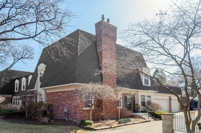 view of property exterior with fence, roof with shingles, an attached garage, brick siding, and a chimney