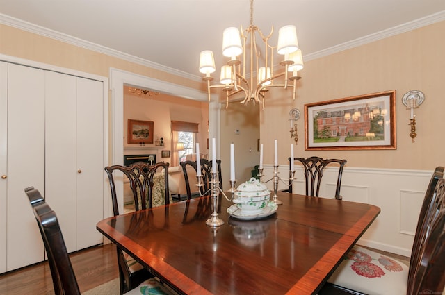 dining space with crown molding, dark wood-type flooring, a chandelier, wainscoting, and a fireplace