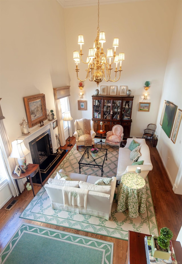 living area with wood finished floors, visible vents, a high ceiling, a fireplace with raised hearth, and a notable chandelier