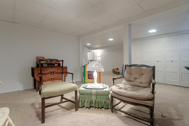 living area with a paneled ceiling and carpet flooring