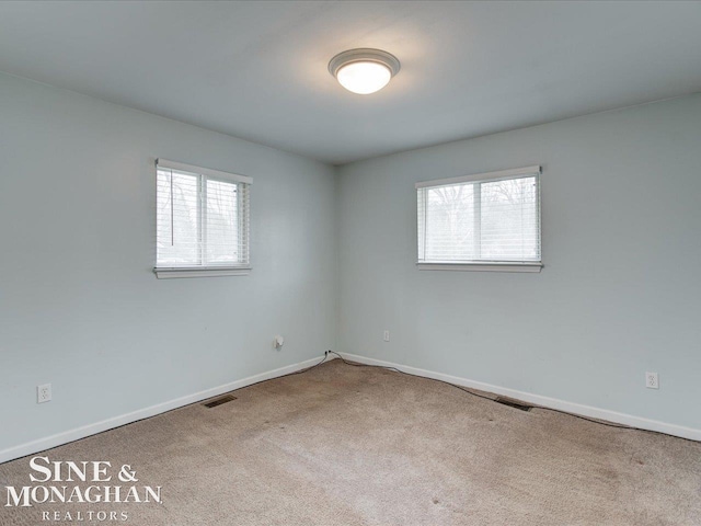 unfurnished room featuring plenty of natural light, carpet, visible vents, and baseboards