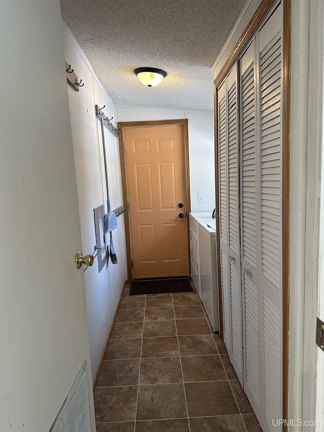 hall with a textured ceiling, dark tile patterned flooring, visible vents, and washing machine and clothes dryer