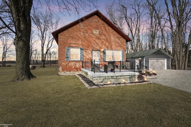 back of property at dusk featuring a yard, an outbuilding, brick siding, and a garage