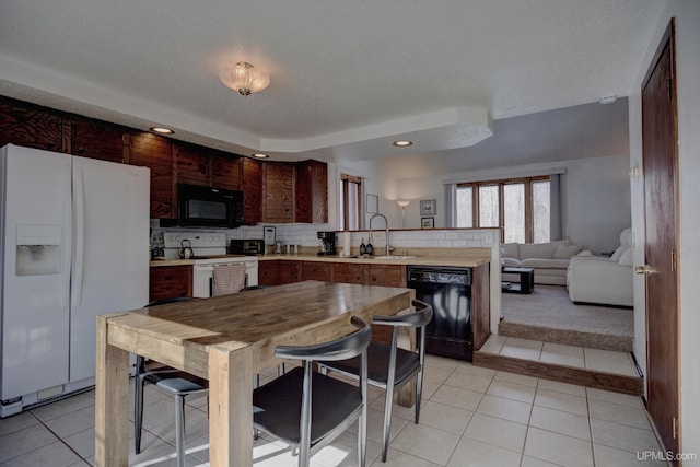 kitchen with light countertops, light tile patterned floors, a peninsula, black appliances, and a sink