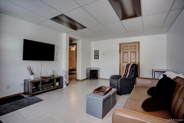 living area with baseboards, a paneled ceiling, light tile patterned flooring, and a wood stove