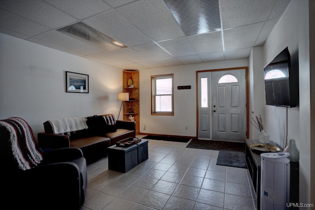 living area with tile patterned floors, a drop ceiling, and baseboards