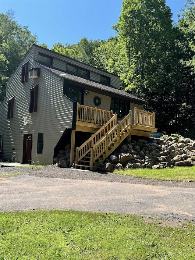 view of front facade with a wall mounted air conditioner, aphalt driveway, a wooden deck, and stairs