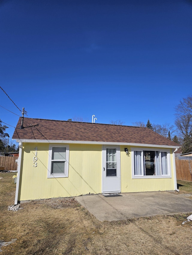 rear view of property featuring a shingled roof, a patio, and fence