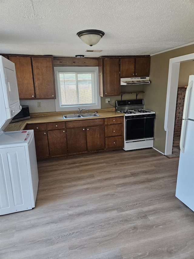 kitchen featuring under cabinet range hood, a sink, stacked washing maching and dryer, freestanding refrigerator, and range with gas cooktop