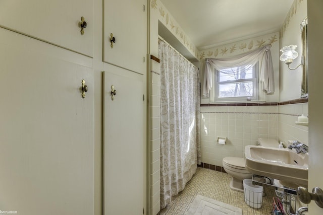 full bathroom with a wainscoted wall, a sink, tile patterned flooring, tile walls, and toilet