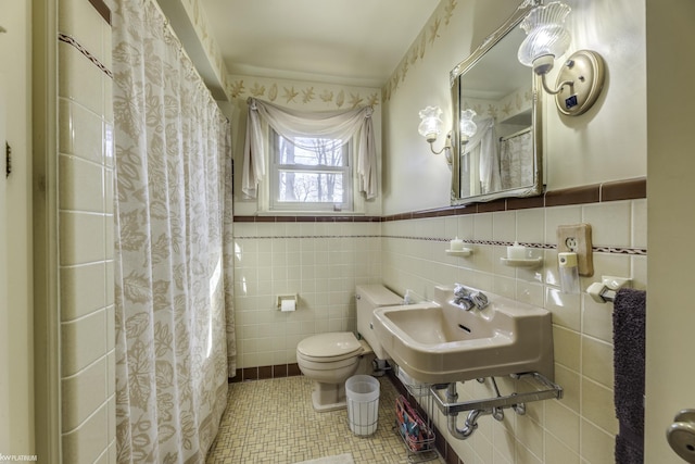 full bath featuring a wainscoted wall, a sink, tile walls, toilet, and tile patterned floors