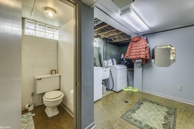 bathroom featuring washer and dryer, baseboards, toilet, and concrete block wall