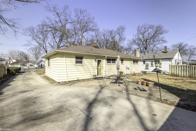 back of house featuring concrete driveway, roof with shingles, a patio, and fence