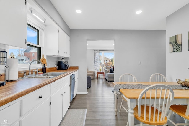 kitchen with recessed lighting, a sink, white cabinets, light wood-style floors, and stainless steel dishwasher