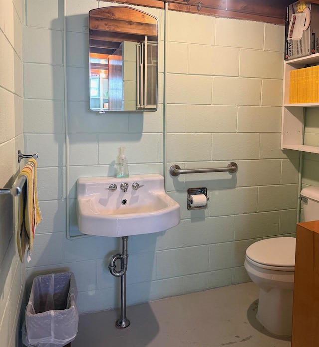 half bathroom featuring concrete flooring, toilet, and concrete block wall