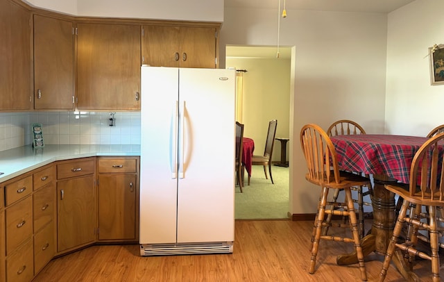 kitchen featuring freestanding refrigerator, decorative backsplash, light countertops, light wood-style floors, and brown cabinets