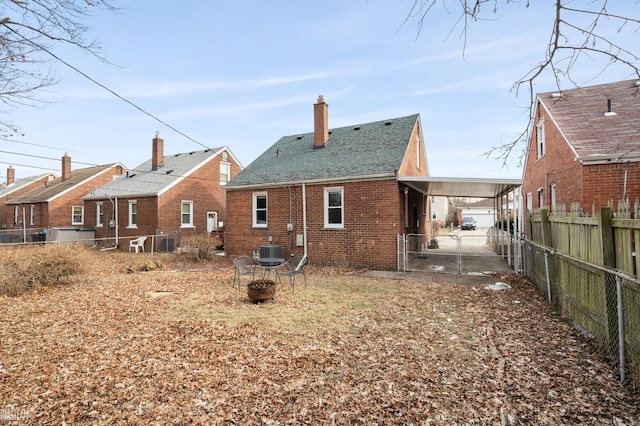 rear view of property with a carport, fence, a fire pit, brick siding, and a chimney