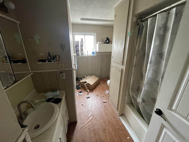 full bath featuring toilet, a sink, a textured ceiling, wood finished floors, and wainscoting