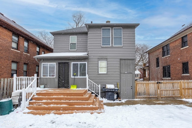 snow covered rear of property with a deck and fence