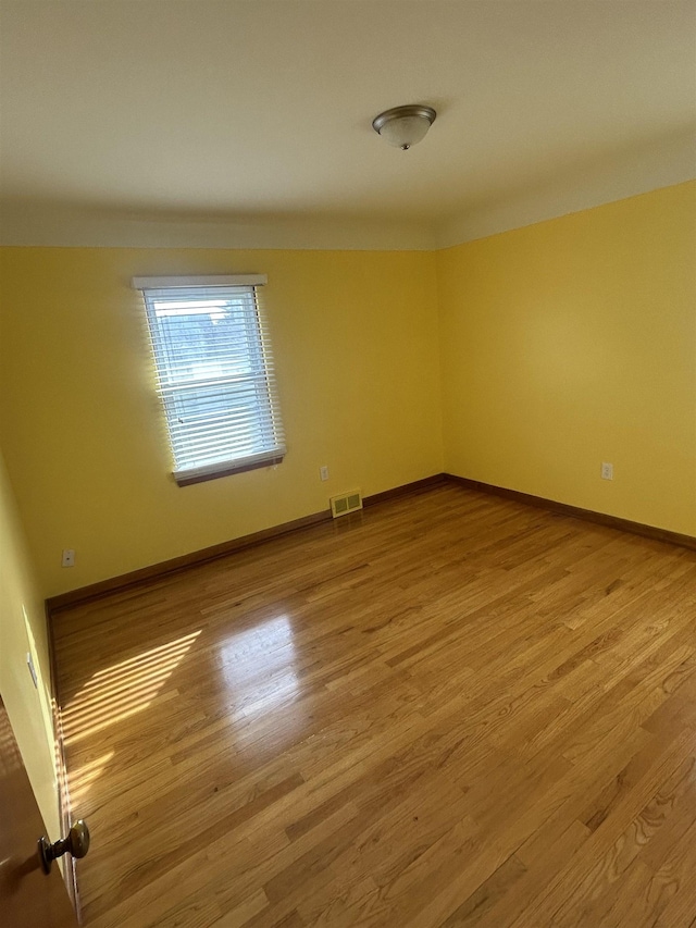 spare room featuring wood finished floors, visible vents, and baseboards