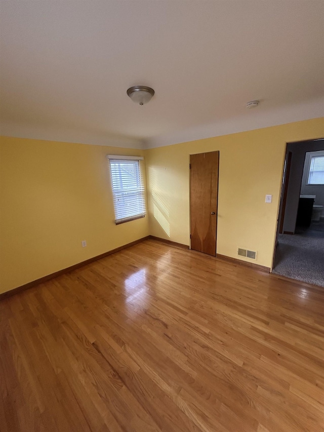 empty room with visible vents, a healthy amount of sunlight, light wood-style flooring, and baseboards