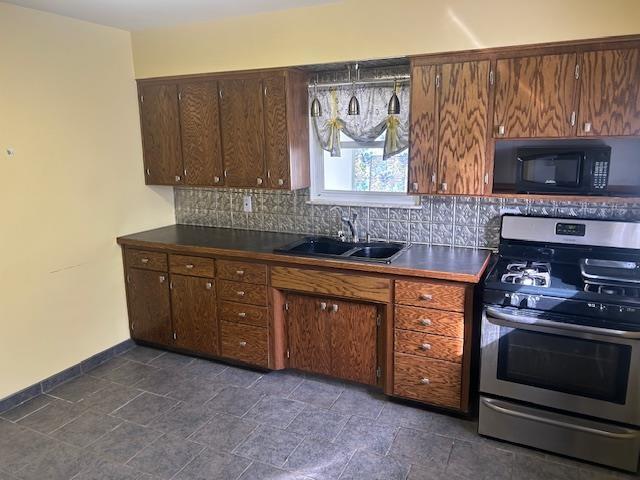 kitchen with a sink, decorative backsplash, black microwave, dark countertops, and stainless steel gas stove