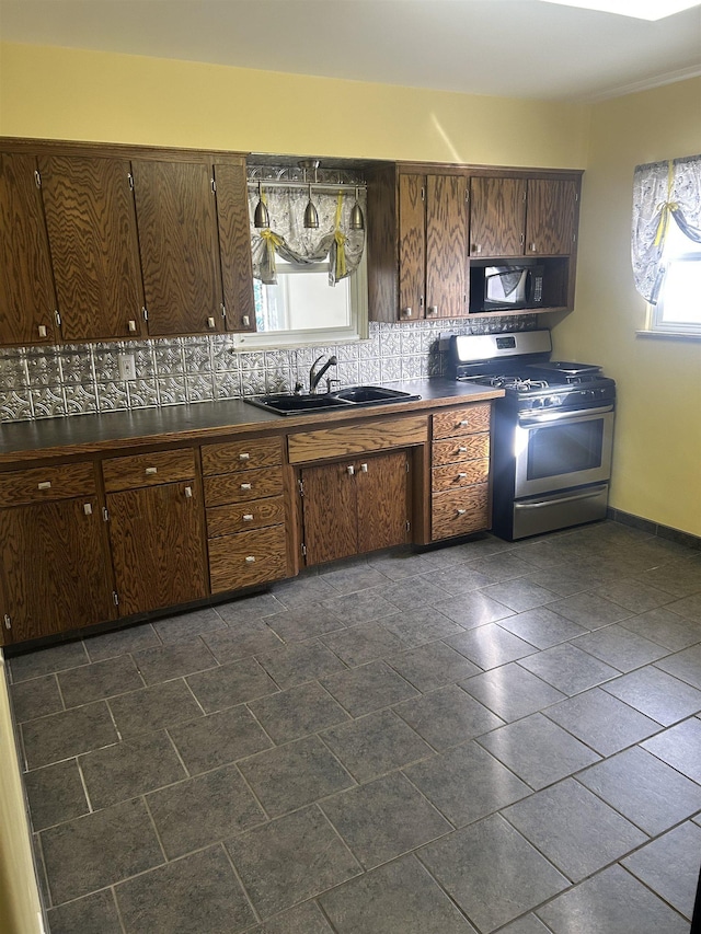 kitchen with dark countertops, black microwave, stainless steel range with gas stovetop, decorative backsplash, and a sink