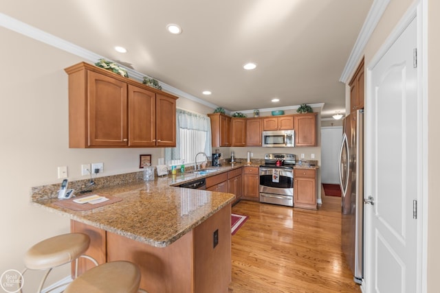 kitchen featuring ornamental molding, light stone counters, appliances with stainless steel finishes, a peninsula, and a sink