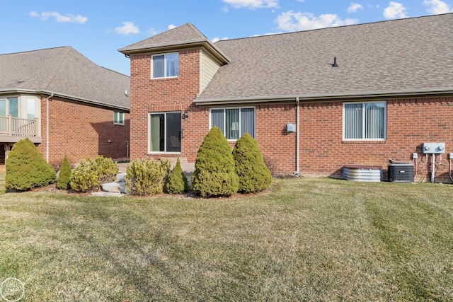 rear view of property featuring cooling unit, a lawn, brick siding, and a shingled roof