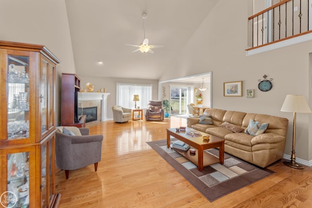 living area with high vaulted ceiling, a ceiling fan, a fireplace, light wood finished floors, and baseboards