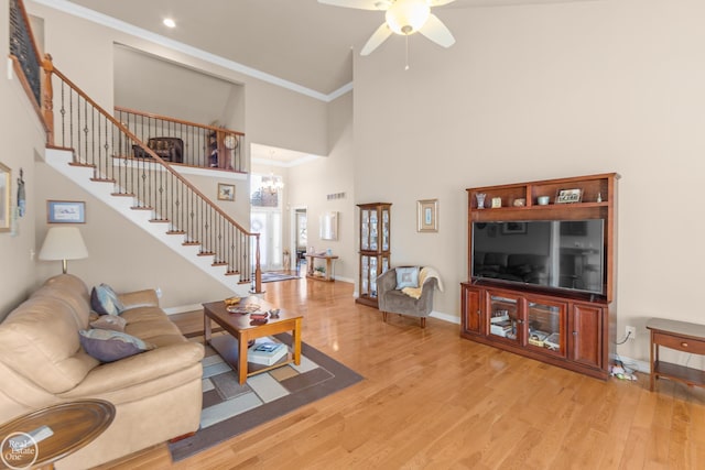 living room with baseboards, light wood-style flooring, a high ceiling, stairs, and crown molding