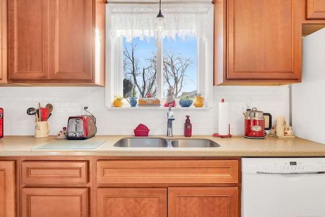 kitchen featuring tasteful backsplash, brown cabinetry, dishwasher, hanging light fixtures, and a sink