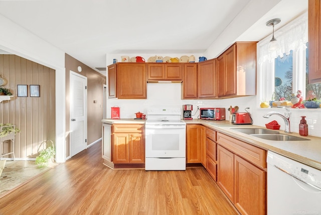 kitchen featuring light wood-type flooring, pendant lighting, a sink, white appliances, and light countertops