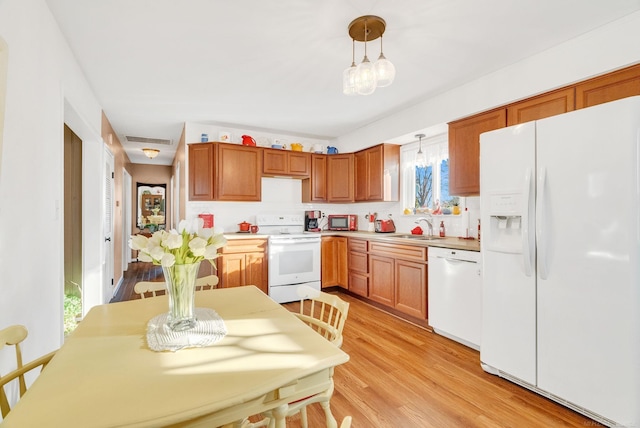 kitchen featuring white appliances, a sink, light countertops, decorative light fixtures, and light wood-type flooring