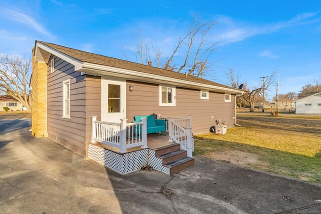 rear view of property featuring a lawn, roof with shingles, and a wooden deck