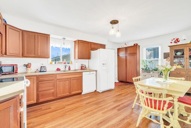 kitchen with light wood-style flooring, a sink, white appliances, light countertops, and hanging light fixtures