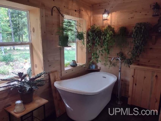 bathroom featuring a soaking tub, wooden walls, and a wealth of natural light