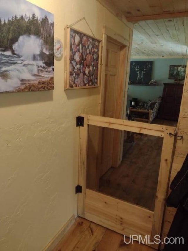 hall featuring wooden ceiling, wood finished floors, baseboards, and a textured wall