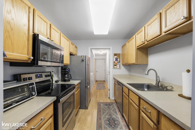 kitchen with light brown cabinetry, stainless steel appliances, light wood-style floors, and a sink