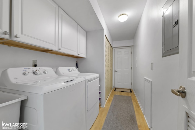 washroom featuring baseboards, washing machine and clothes dryer, light wood-style flooring, electric panel, and cabinet space