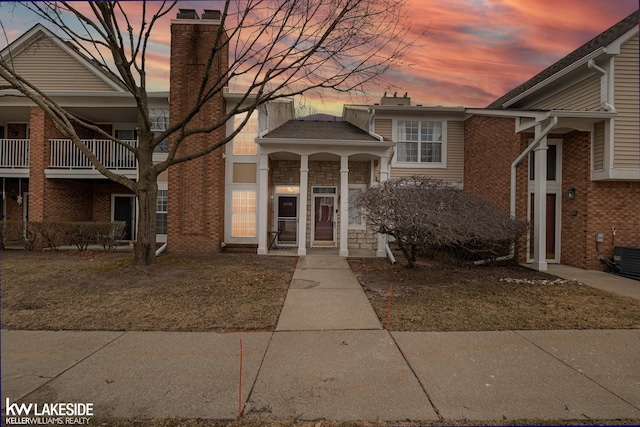 view of front of home with brick siding, stone siding, central AC unit, and a chimney