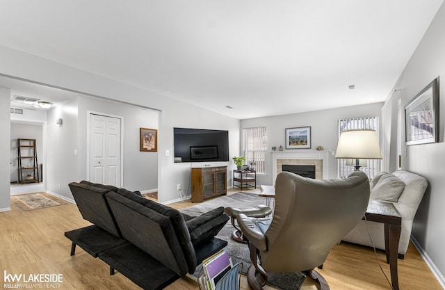 living room with a tiled fireplace, visible vents, light wood-type flooring, and baseboards