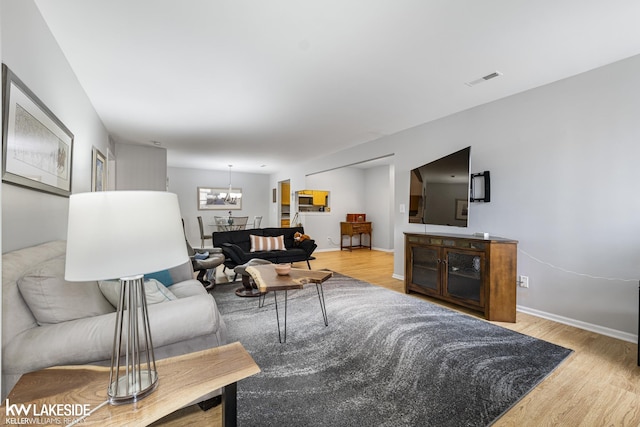 living room featuring baseboards, wood finished floors, visible vents, and a chandelier