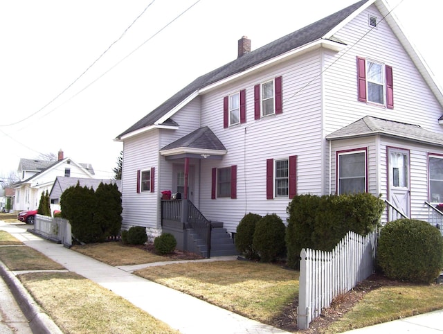 view of front facade with a front yard, a chimney, and fence