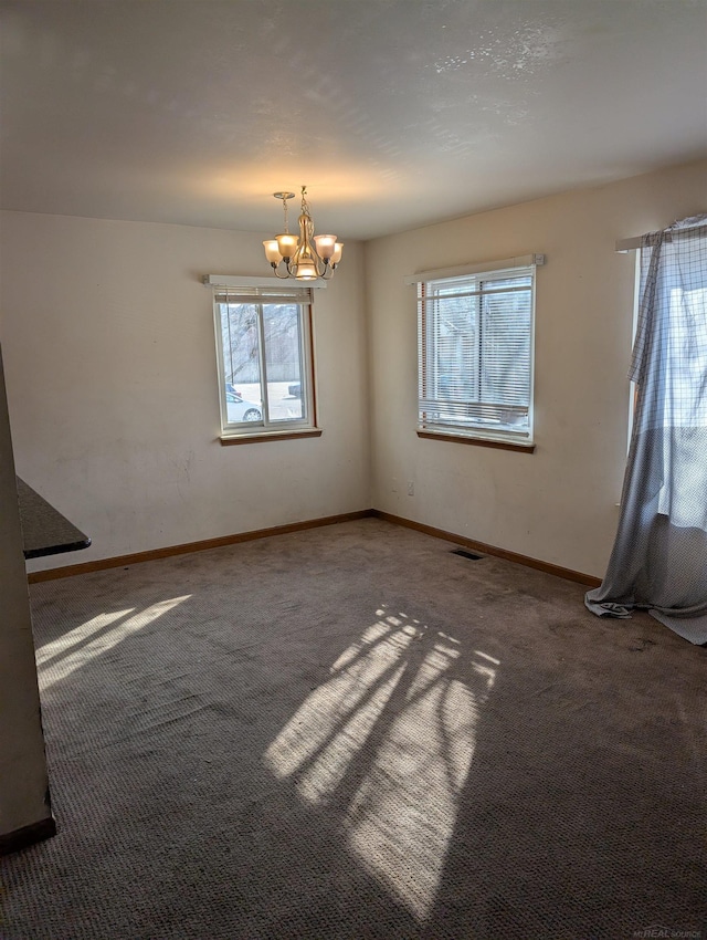 unfurnished room with an inviting chandelier, carpet flooring, visible vents, and baseboards