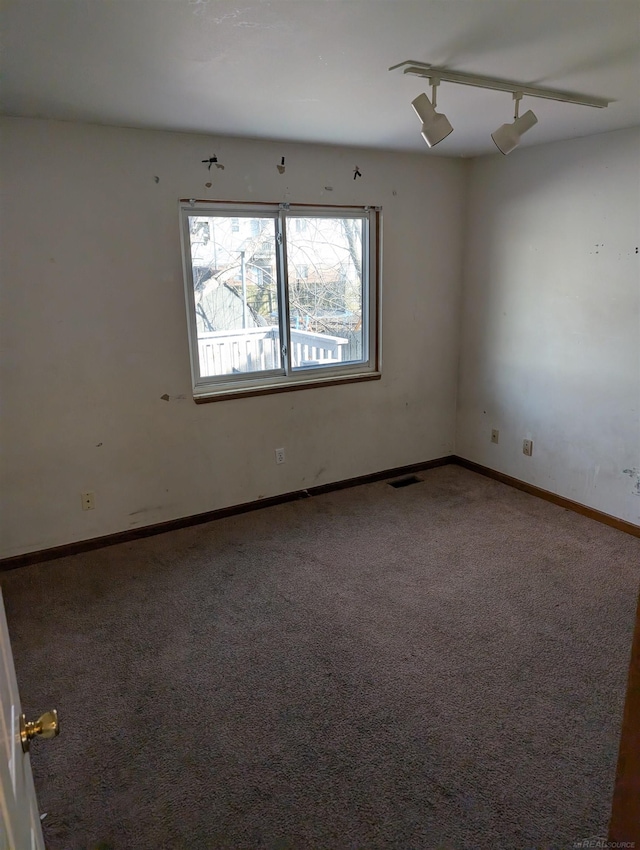 spare room with visible vents, rail lighting, baseboards, and carpet