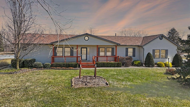 single story home featuring a porch, a shingled roof, and a yard