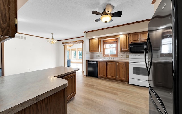 kitchen featuring visible vents, a sink, black appliances, light wood-style floors, and tasteful backsplash