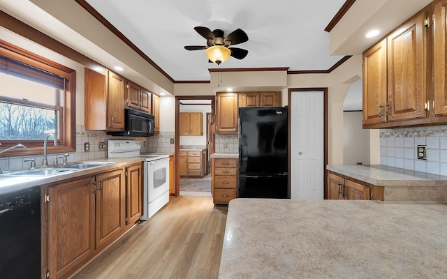 kitchen featuring black appliances, ornamental molding, light countertops, and a sink