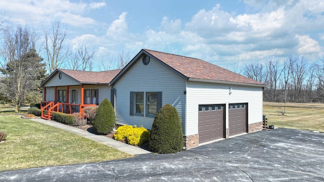 view of side of home with a garage, a porch, a shingled roof, and a yard